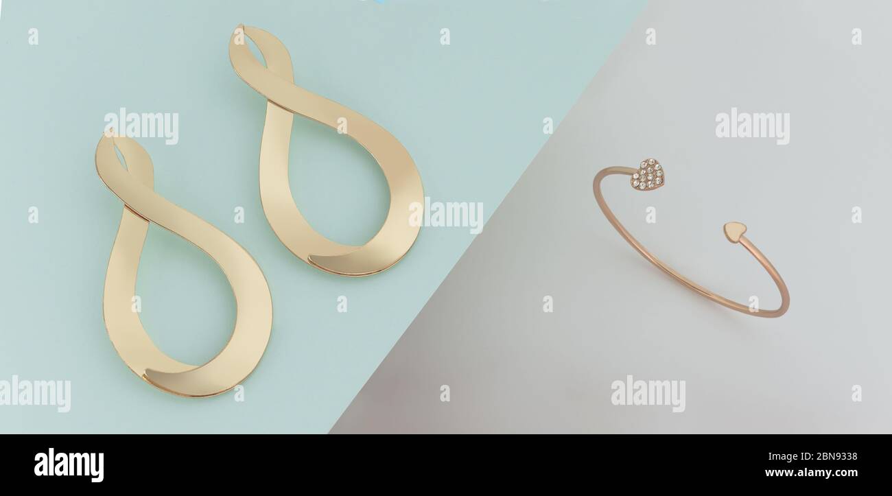 Paire de boucles d'oreilles dorées modernes et bracelet sur papier bleu sur fond blanc Banque D'Images