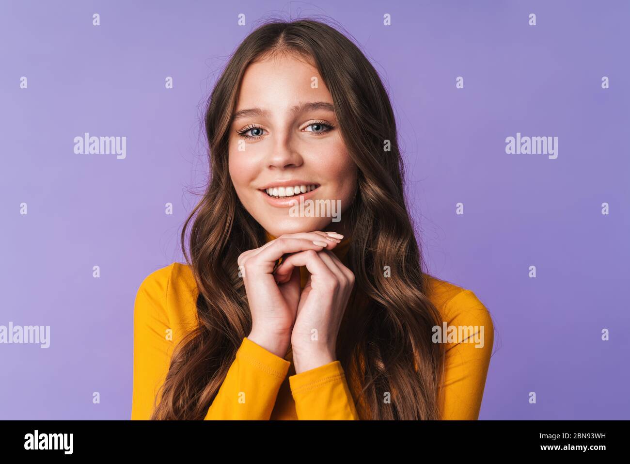 Image de jeune belle femme avec de longs cheveux bruns souriant et posant à la caméra isolée sur fond violet Banque D'Images