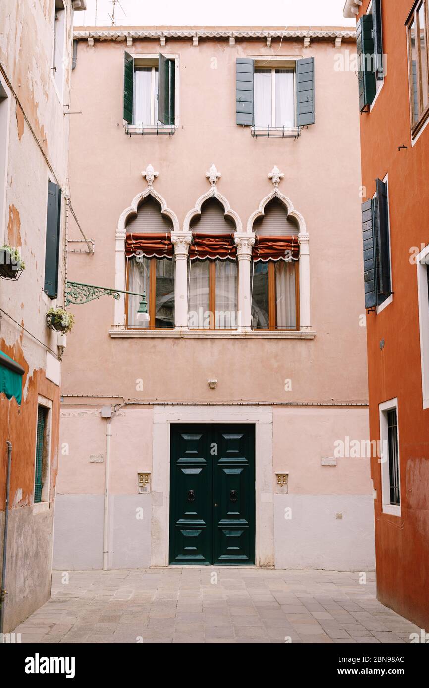 Façade d'une maison de pêche de trois étages à Venise, Italie. Porte avant en bois vert massif, trois fenêtres vénitiennes classiques avec un haut pointu, des colonnes et Banque D'Images