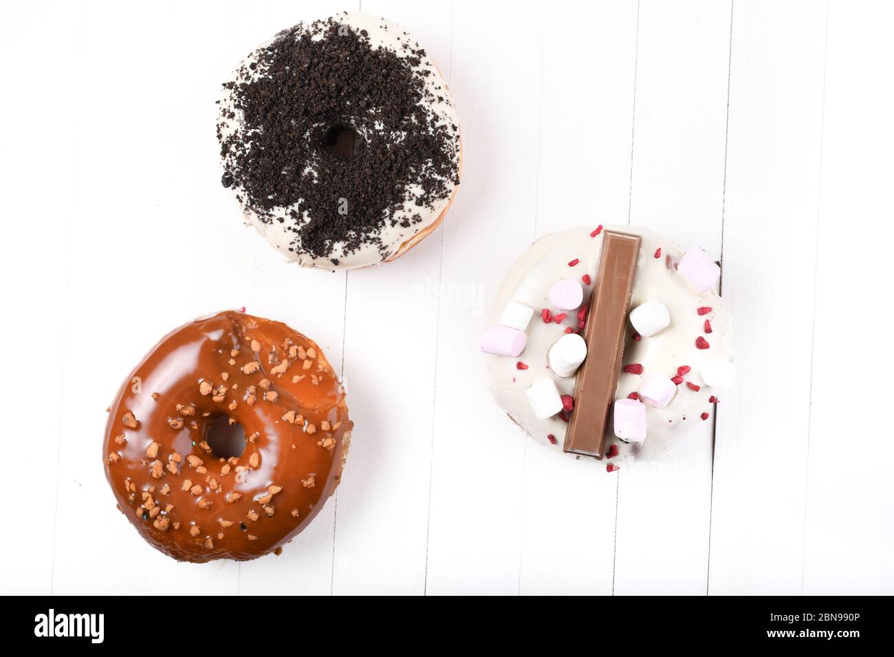 Trois fondus émaillés de chocolat noir et blanc, marshmallows, biscuit crumbles, beignets enrobés de sucre caramel sur bois blanc Banque D'Images