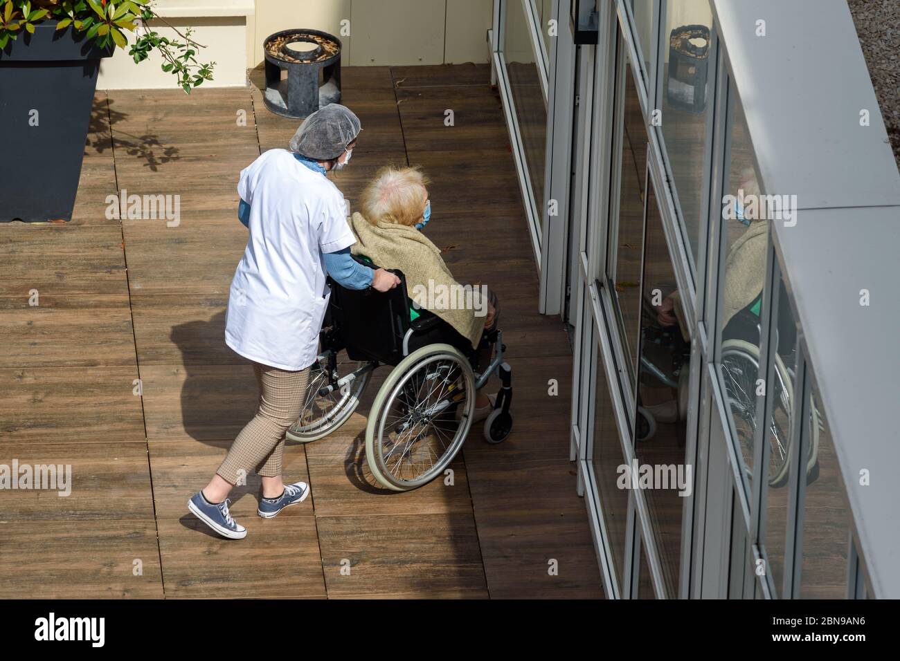 Infirmière prenant soin d'une femme âgée et handicapée dans une maison de soins pendant une journée ensoleillée pendant la pandémie du coronavirus Covid-19. Les deux portent un masque. Banque D'Images