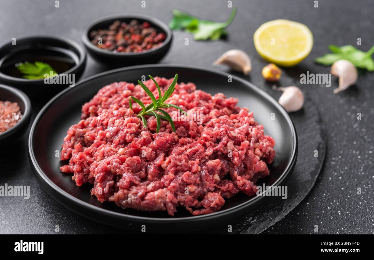 Viande hachée de bœuf haché fraîche sur une assiette noire sur fond de pierre. Banque D'Images