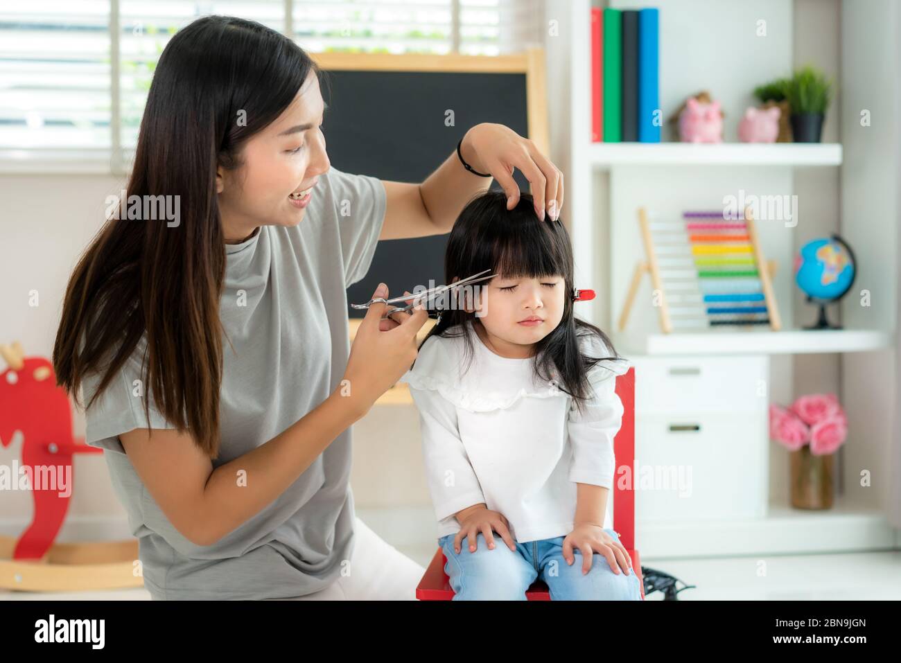 Mère asiatique coupant les cheveux à sa fille dans le salon à la maison tout en restant à la maison à l'abri du coronavirus Covid-19 pendant le verrouillage. Mise en quarantaine automatique d'un Banque D'Images