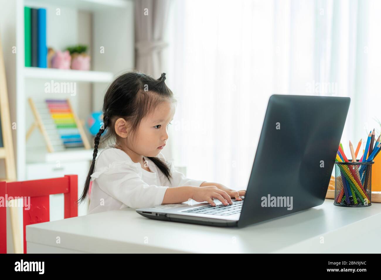École maternelle asiatique de fille vidéo conférence e-learning avec enseignant sur ordinateur portable dans le salon à la maison. Homeschooling et l'apprentissage à distance, en ligne Banque D'Images