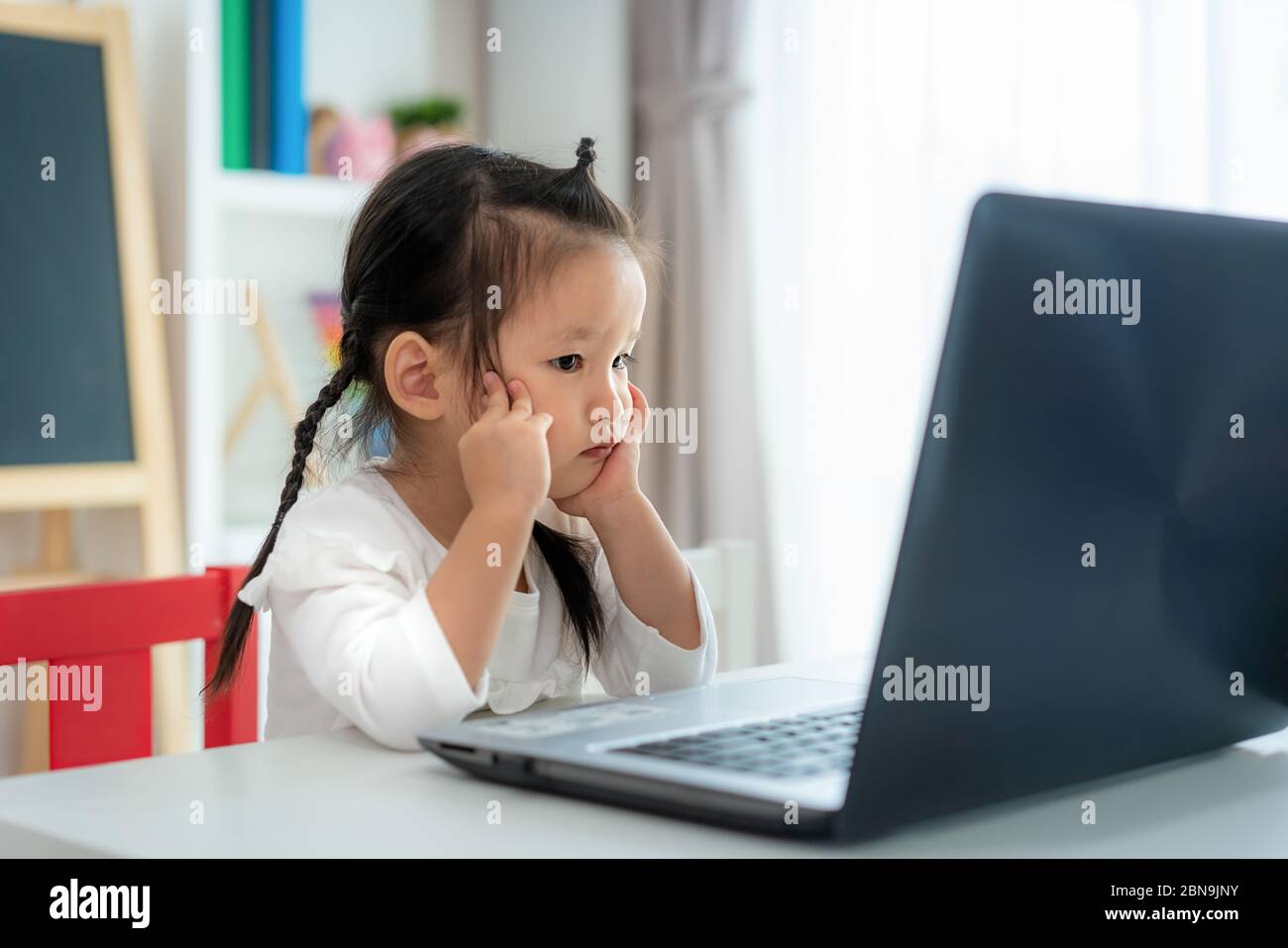 École maternelle asiatique de fille vidéo conférence e-learning avec enseignant sur ordinateur portable dans le salon à la maison. Homeschooling et l'apprentissage à distance, en ligne Banque D'Images