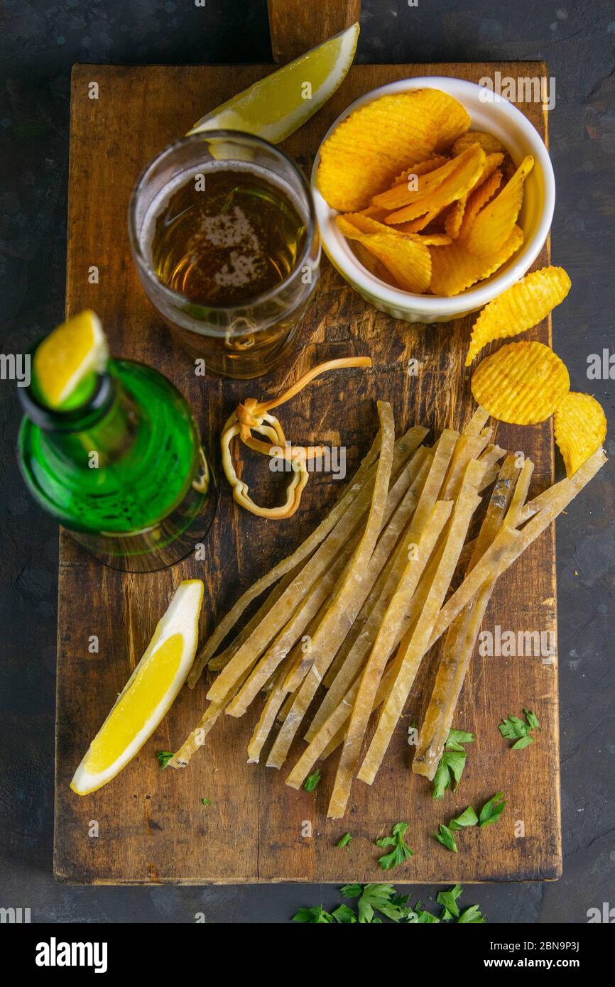 Collation d'élite au thon salé séché avec bière, citron et chips de pommes de terre sur un panneau en bois sombre. En-cas sur le poisson avec de la bière. Vues de dessus, gros plan Banque D'Images