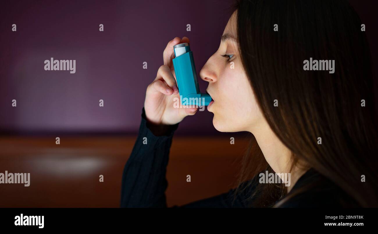 Femme inhalant un inhalateur bleu d'asthme à la maison. Asthme et coronavirus concept. Banque D'Images