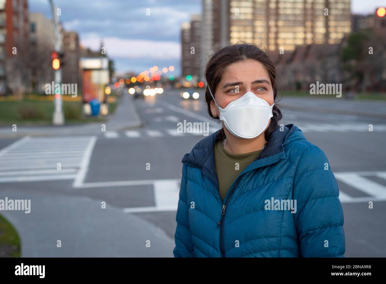 Concept du coronavirus pandémique Covid-19. Jeune belle femme dans le masque médical protecteur debout sur la rue par la route. Banque D'Images