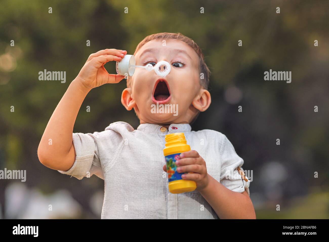 Un enfant à la bouche ouverte et aux yeux larges souffle des bulles de savon colorées dans la nature. Banque D'Images