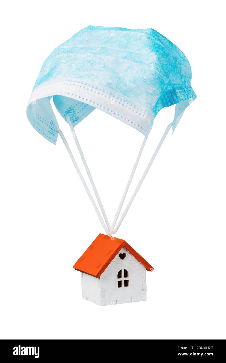 Une maison de jouets vole sur un parachute à partir d'un masque médical, isolé sur un fond blanc. Concept de sortie de quarantaine Banque D'Images