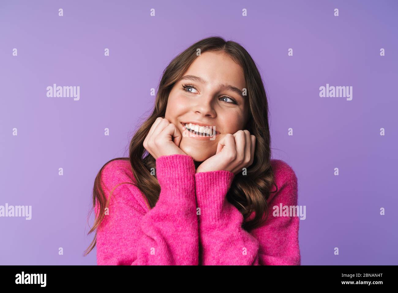 Image de jeune belle femme avec de longs cheveux bruns souriant et touchant son visage isolé sur fond violet Banque D'Images