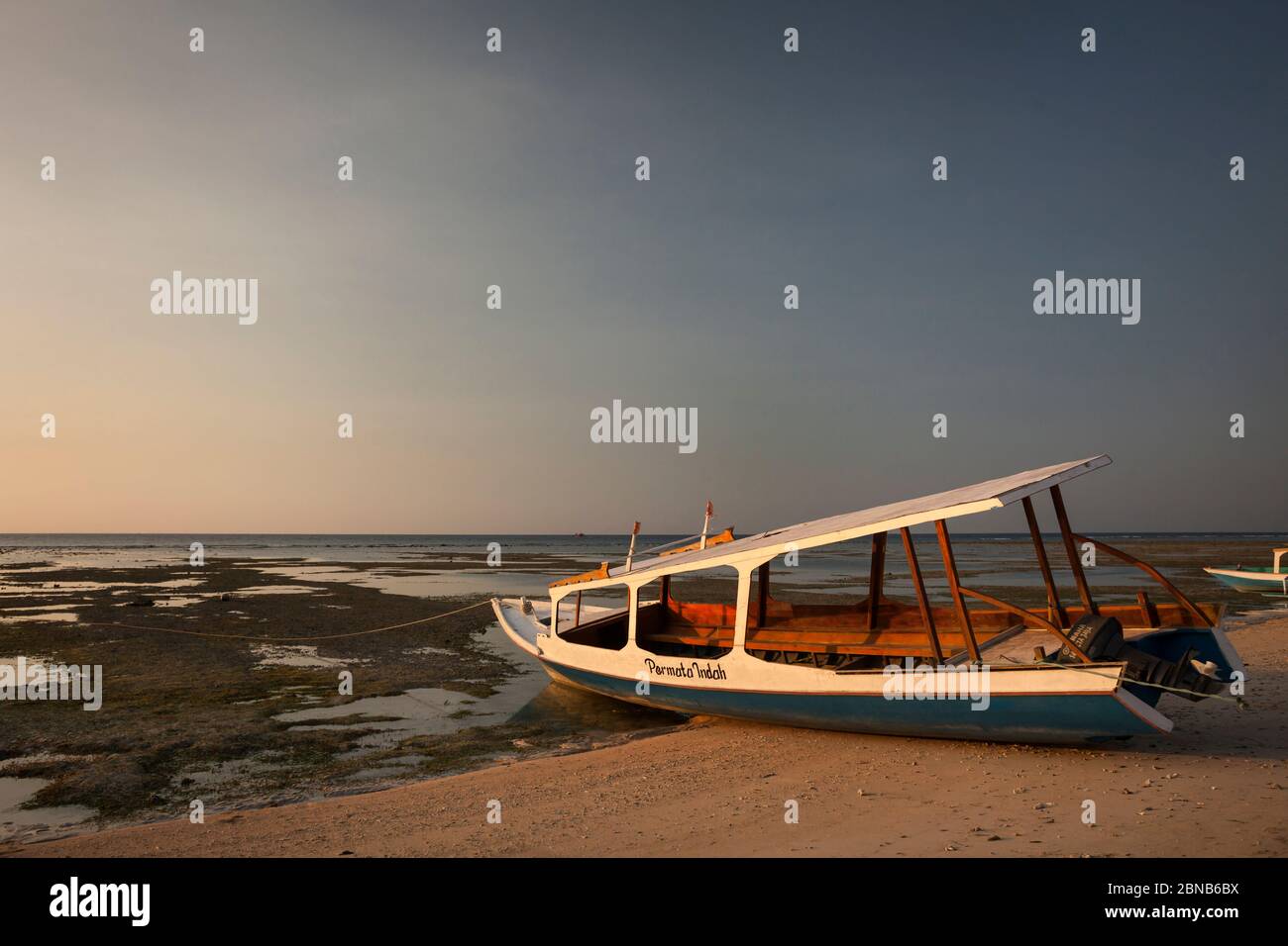 Vue horizontale au coucher du soleil d'un bateau incliné s'agrest sur la plage en raison de la marée basse, Gili Air, îles Gili, Indonésie Banque D'Images