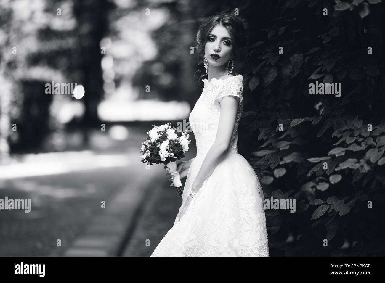 La mariée dans une robe de mariage blanche tient un bouquet sur un fond de parc vert Banque D'Images