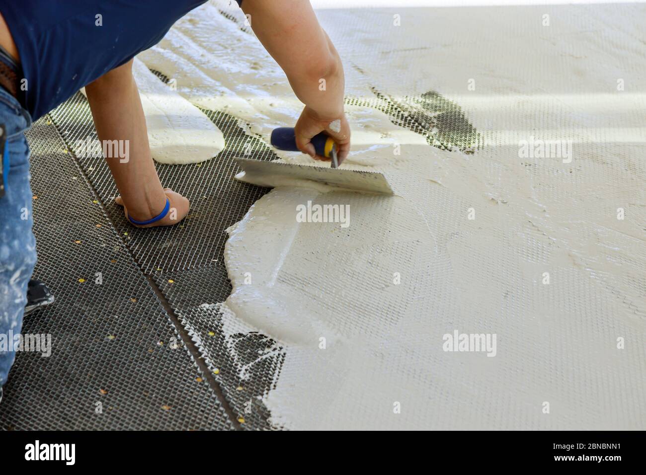 Un ouvrier de la construction truroweling mortier sur un sol en béton en préparation pour la pose de carreaux de plancher. Banque D'Images