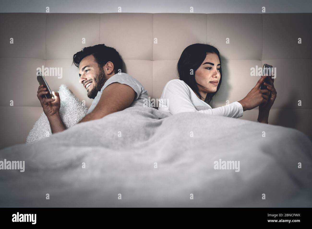 Jeune couple allongé dans le lit en utilisant le téléphone mobile tout en  ignorant les uns les autres - l'homme et la femme accro à la technologie  des réseaux sociaux de smartphone