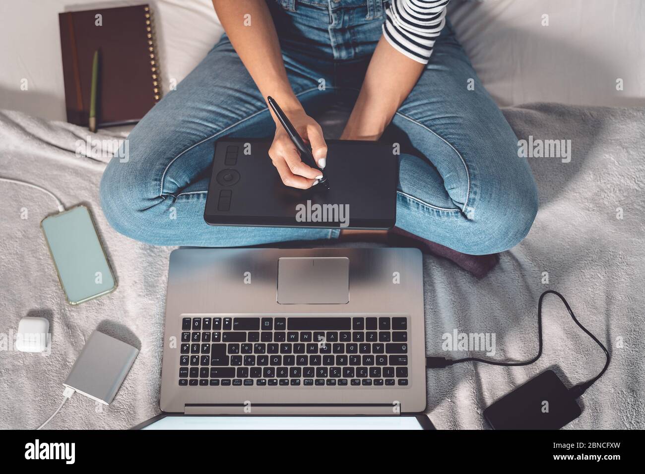 Graphiste femme intelligente travaillant sur ordinateur à la maison - jeune femme dessin avec stylo interactif et ordinateur portable dans le lit Banque D'Images
