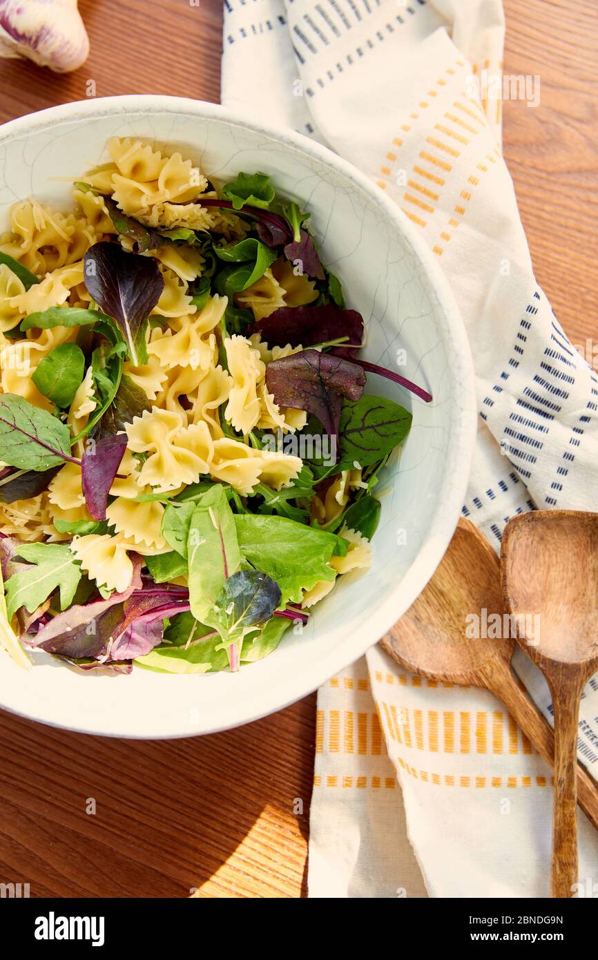 Vue de dessus du bol avec ingrédients pour salade de pâtes avec spatules, serviette et ail sur fond de bois Banque D'Images