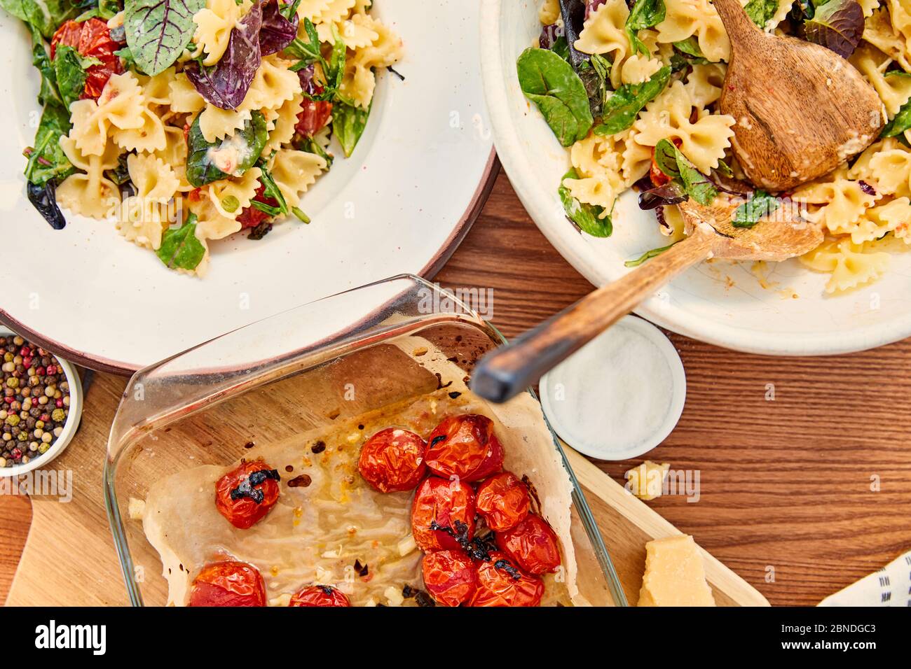 Vue de dessus de l'assiette et du bol avec salade de pâtes et spatules près de la planche à découper et du plat à pâtisserie avec les ingrédients sur fond de bois Banque D'Images