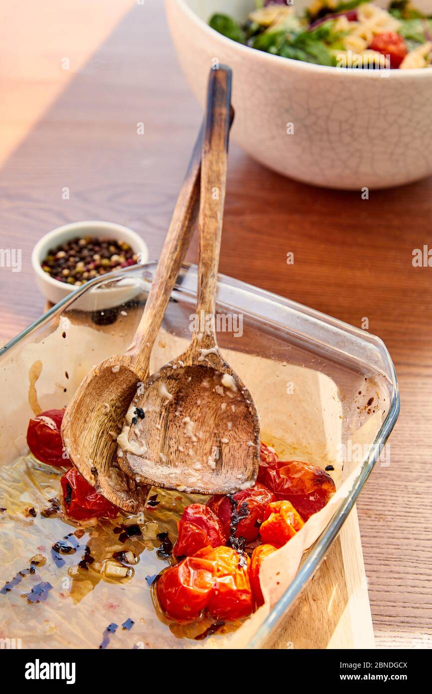 Vue en grand angle du plat de cuisson avec spatules et tomates sur le plan de coupe près des bols avec salade de poivre et de pâtes sur fond de bois Banque D'Images