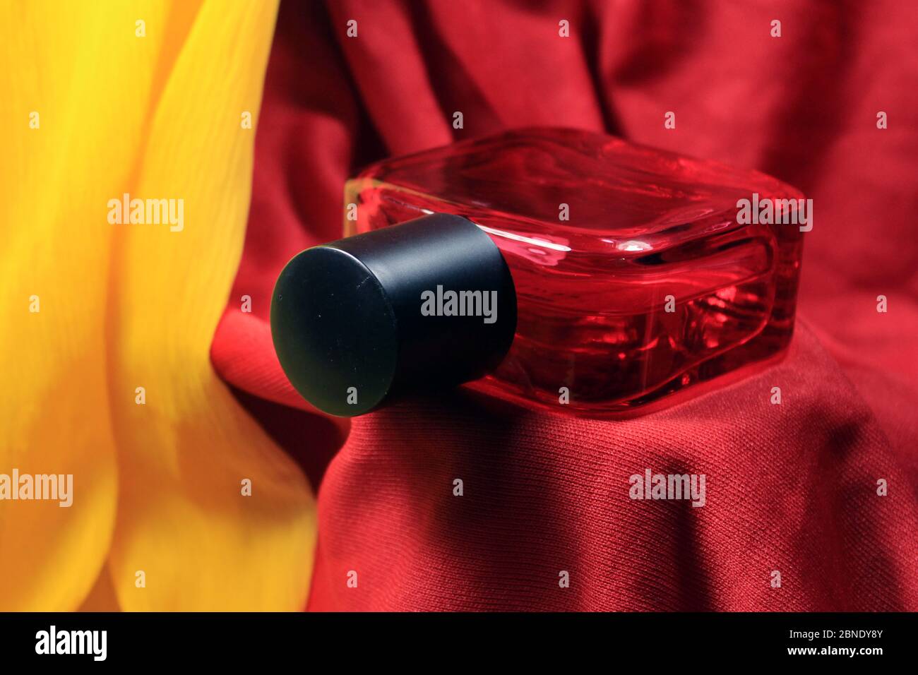 Bouteille de parfum rouge homme de couleur isolée sur fond de soie rouge. Flacon de parfum rouge avec bouchon noir, spray naturel. Banque D'Images