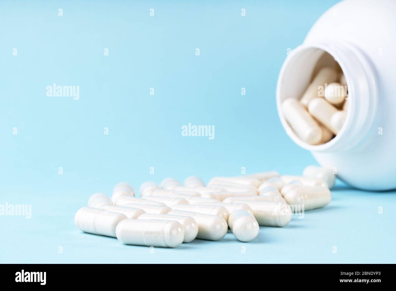 Des pilules et capsules médicales blanches débordent du flacon. Médicament dans un contenant blanc sur fond bleu. Soins de santé, assurance maladie, médecine conc Banque D'Images