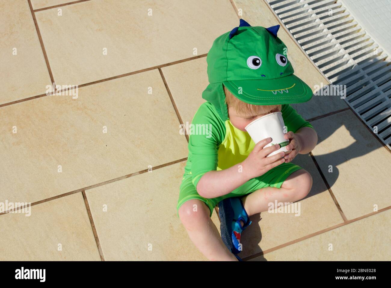 Un petit enfant prend une pause de jouer dans la piscine pour avoir une tasse d'eau Banque D'Images