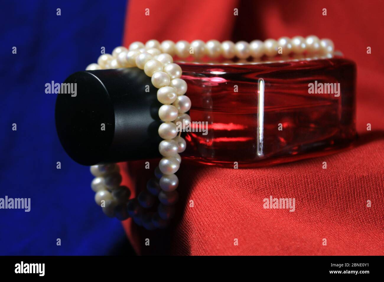 Flacon de parfum rouge homme isolé sur fond bleu et rouge avec accessoires femelles. Banque D'Images