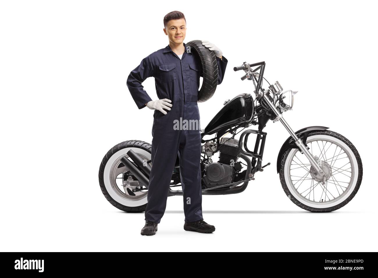 Portrait complet d'un mécanicien portant un pneu et se tenant à côté d'une moto à hacheur isolée sur fond blanc Banque D'Images