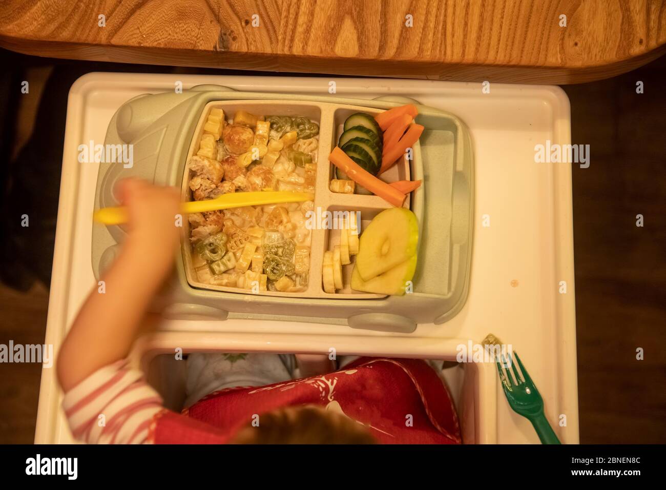 vue de dessus, le tout-petit est assis devant une assiette pour enfants remplie de délicieux aliments appétissants et coupe la nourriture avec un couteau en plastique pour enfants. doux Banque D'Images