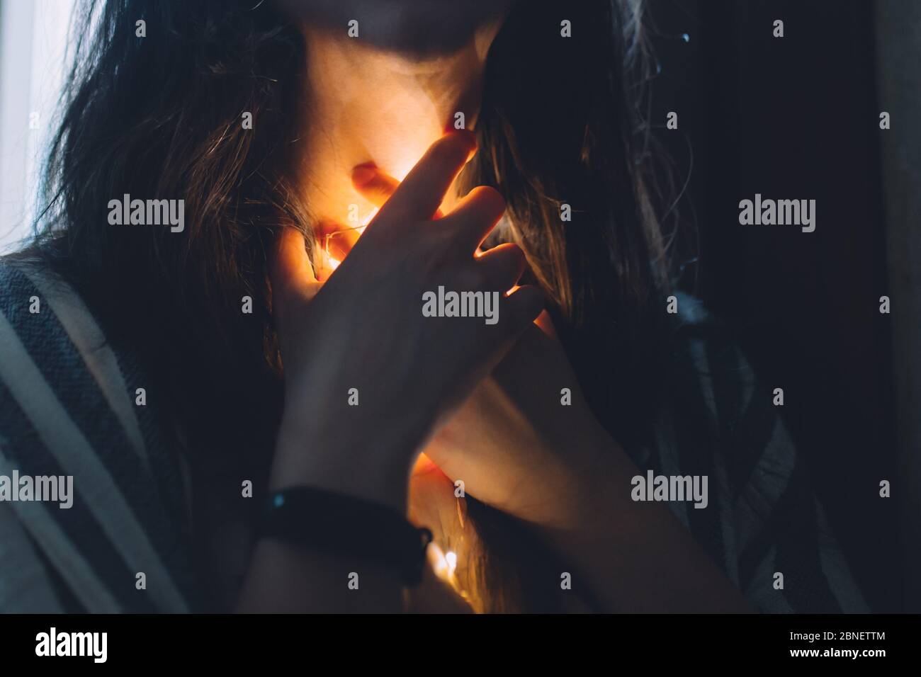 Femme stressée avec une lumière qui brille vers le bas de sa gorge avec une montre intelligente Banque D'Images