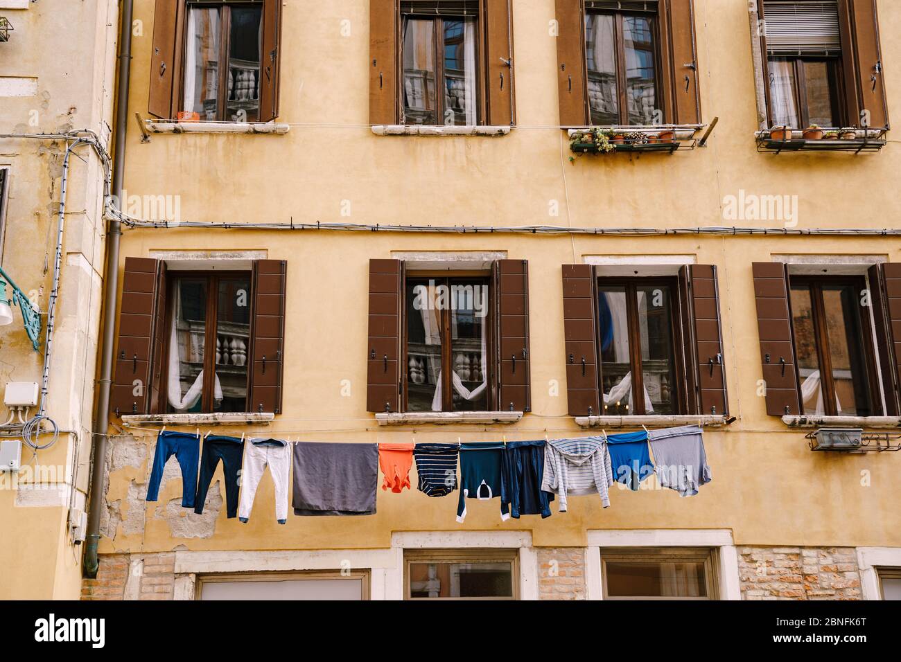 Gros plan de la façade d'un bâtiment, dans les rues de Venise, Italie. Mur en pierre jaune avec volets ouverts sur les fenêtres, marron. Beaucoup de vêtements sont Banque D'Images