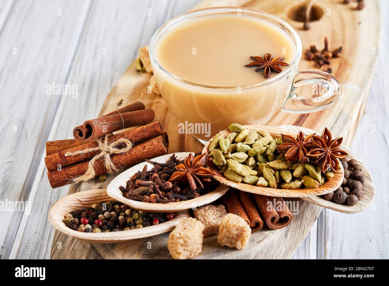 Boisson traditionnelle indienne - thé masala aux épices. Cannelle, cardamome, anis, sucre, clous de girofle, poivre sur fond de bois clair Banque D'Images