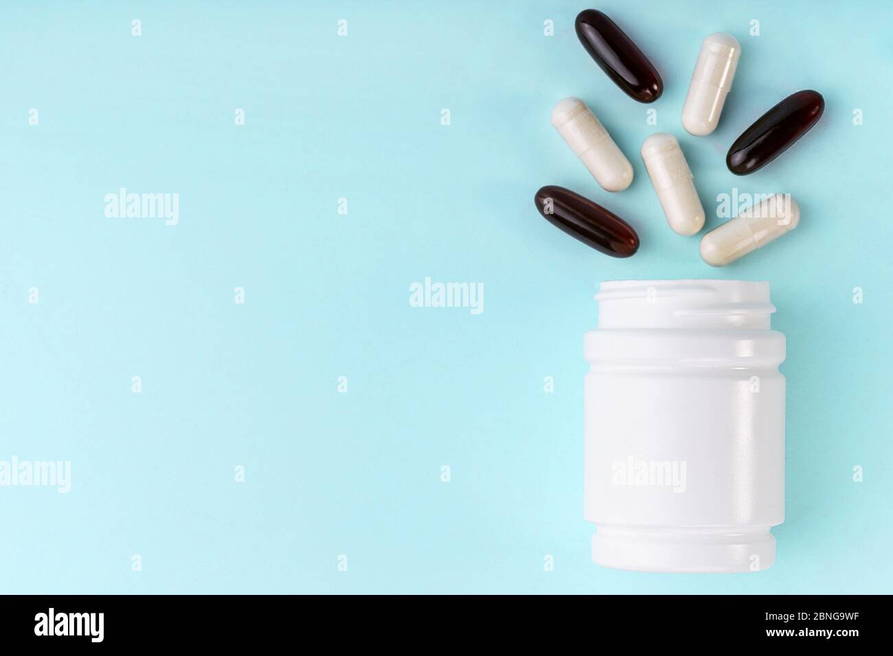 Des pilules et capsules médicales blanches débordent du flacon. Médicament dans un contenant blanc sur fond bleu. Soins de santé, assurance maladie, médecine conc Banque D'Images