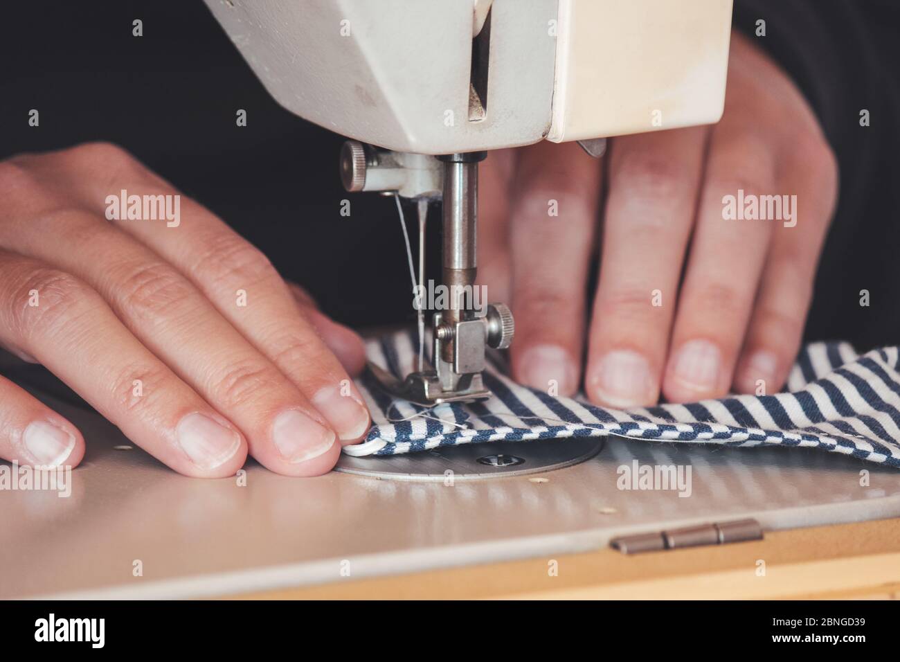 Les mains des femmes utilisant la machine à coudre pour coudre un masque médical coloré du visage pendant la pandémie de coronavirus. Masque de protection fait maison contre le virus. Masques à coudre, COVID-19. Mise au point sélective. Banque D'Images