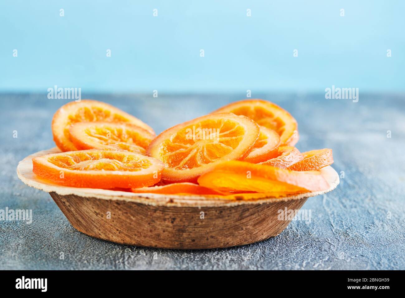 Tranches d'oranges ou de mandarines séchées dans une assiette en bois sur fond bleu. Végétarisme et alimentation saine. Copier l'espace Banque D'Images