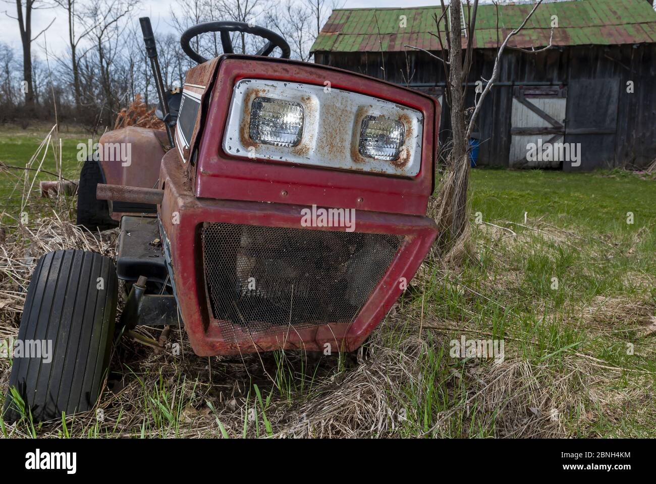 Gros plan d'un vieux tracteur rouge dans un jardin par une maison capturée un jour ensoleillé Banque D'Images