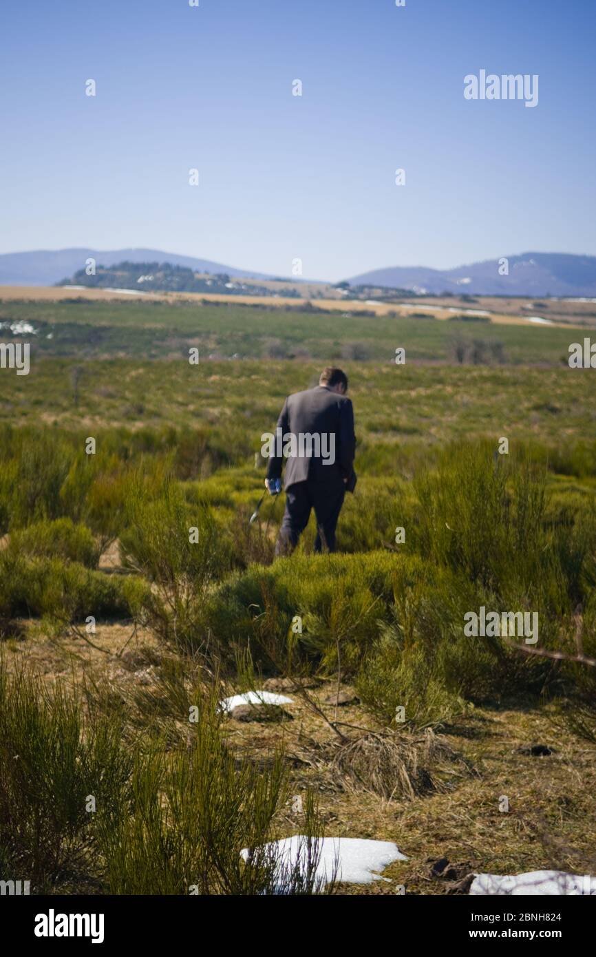 un homme adulte dans un costume sombre avec caméra à la main s'éloigne de la caméra à travers les champs ouverts avec des taches de neige Banque D'Images