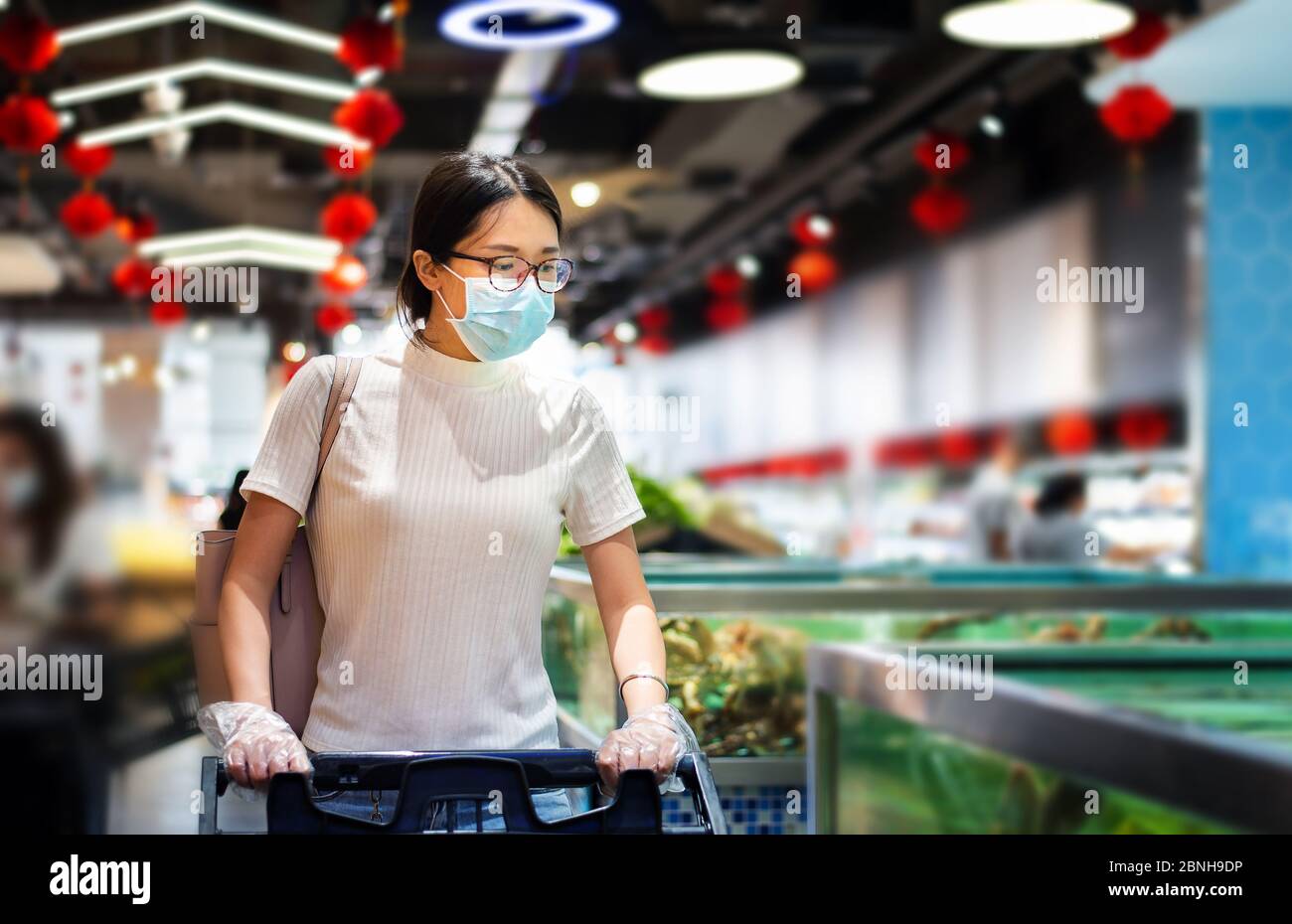 Femme asiatique qui fait ses courses sur le marché, portant un masque et des gants pour prévenir la propagation du virius pendant la pandémie du coronavirus Banque D'Images