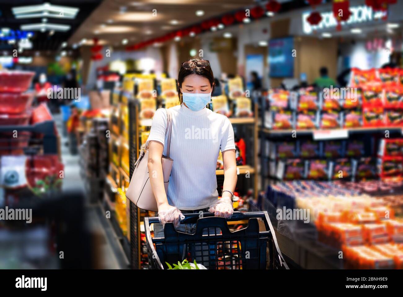 Femme asiatique qui fait ses courses sur le marché porte un masque et pousse le chariot avec des gants pour prévenir la propagation du virus pendant une pandémie de coronavirus Banque D'Images