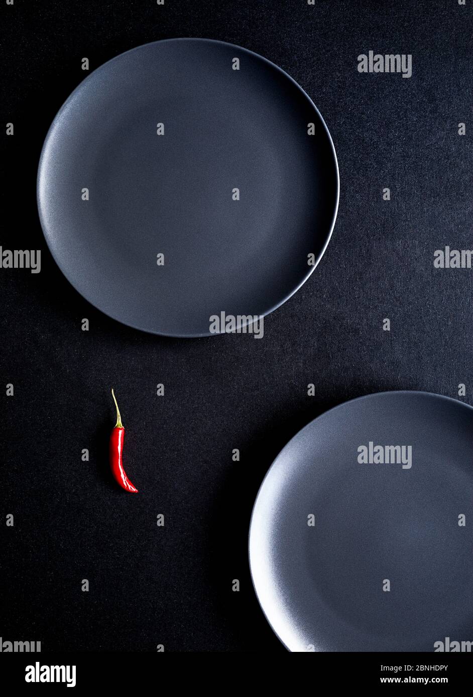 Composition minimaliste de piment rouge et deux assiettes en céramique noire sur table noire Banque D'Images