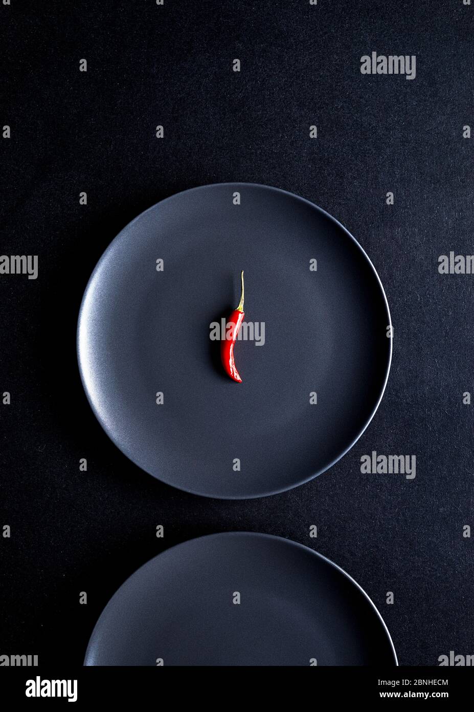 Composition minimaliste de piment rouge dans une plaque en céramique noire sur une table noire Banque D'Images