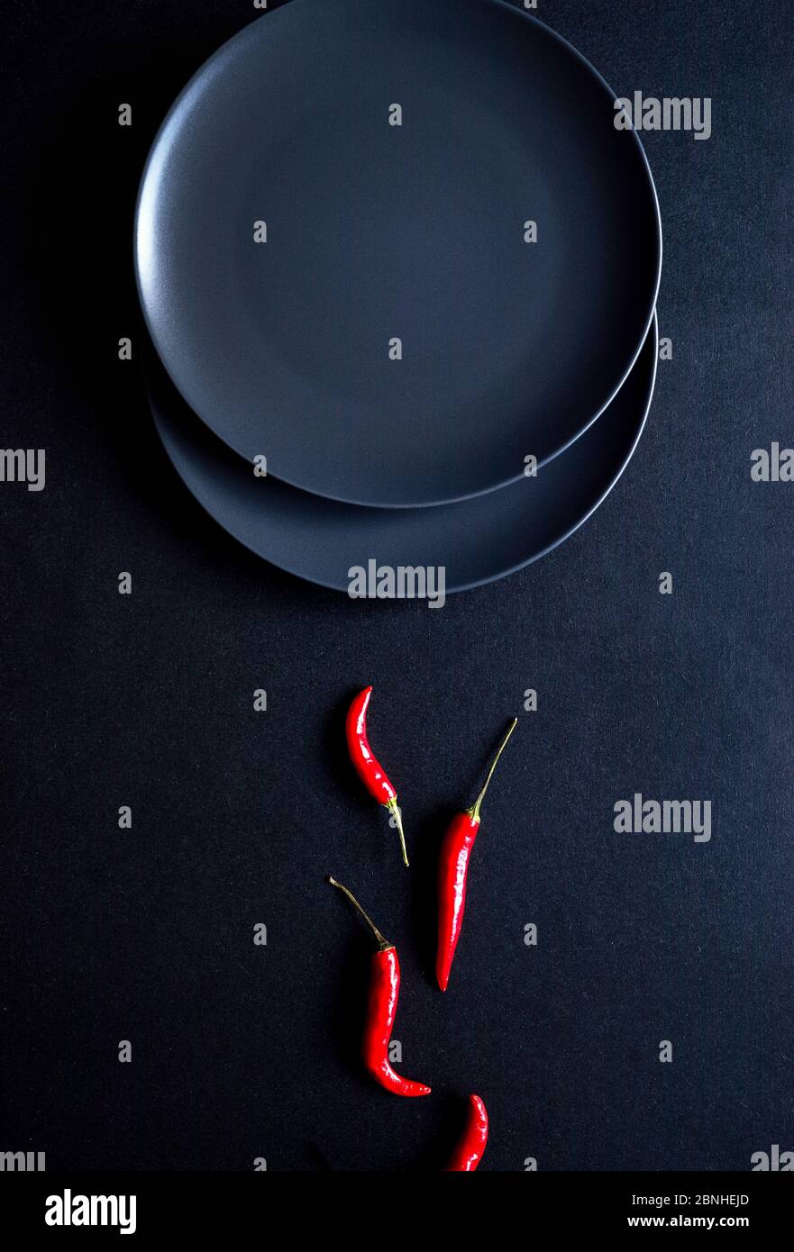 Composition minimaliste de piments rouges et deux assiettes en céramique sur fond noir Banque D'Images