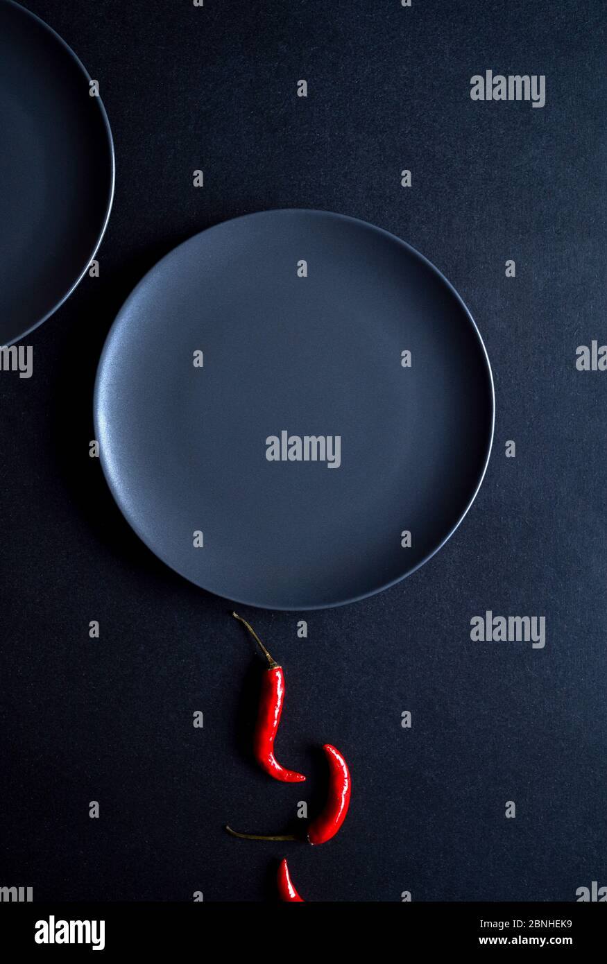 Composition minimaliste de piments rouges et deux assiettes en céramique sur fond noir Banque D'Images