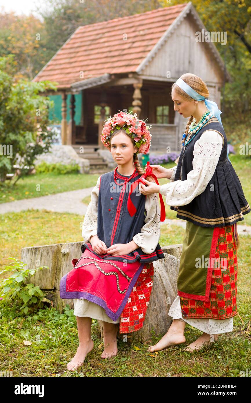 Deux belles filles en vêtements nationaux de la fin du XIXe siècle. Une femme se serpente des rubans dans les cheveux de sa fille. Vieux vêtements. Mise en scène rétro d'un Banque D'Images