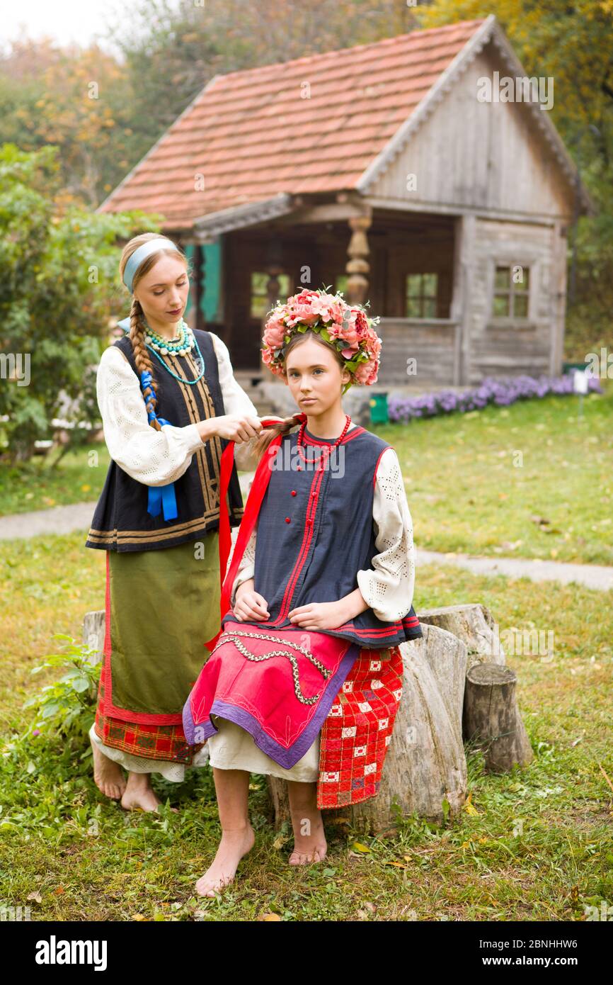 Deux belles filles en vêtements nationaux de la fin du XIXe siècle. Une femme se serpente des rubans dans les cheveux de sa fille. Vieux vêtements. Mise en scène rétro d'un Banque D'Images