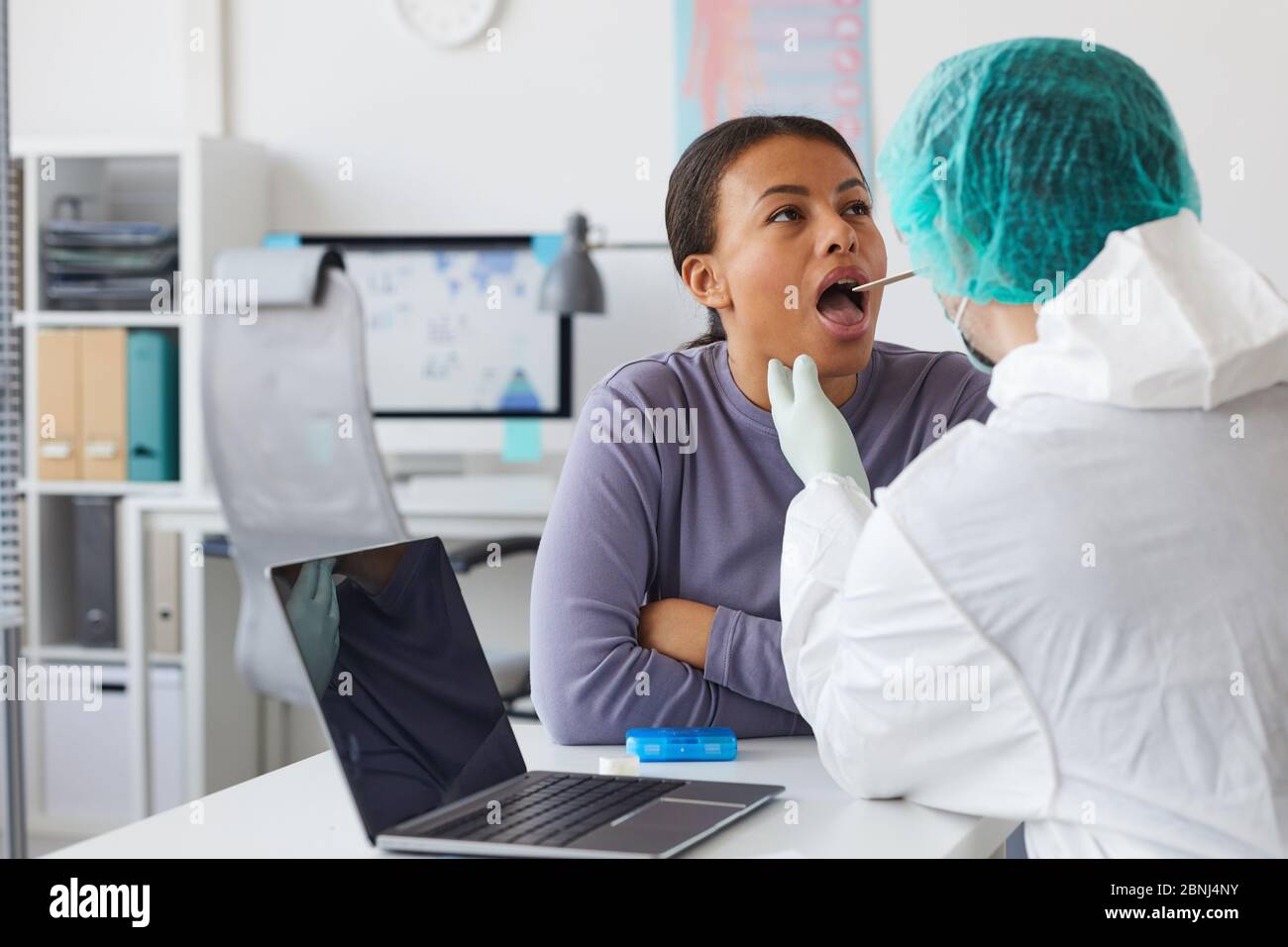 Médecin portant des vêtements de protection examinant la gorge de la femme pendant un examen médical à l'hôpital Banque D'Images