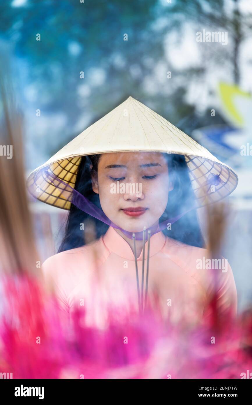 Une jeune femme vietnamienne dans un chapeau conique faisant des offrandes d'encens à un temple bouddhiste, Hue, Vietnam, Indochine, Asie du Sud-est, Asie Banque D'Images