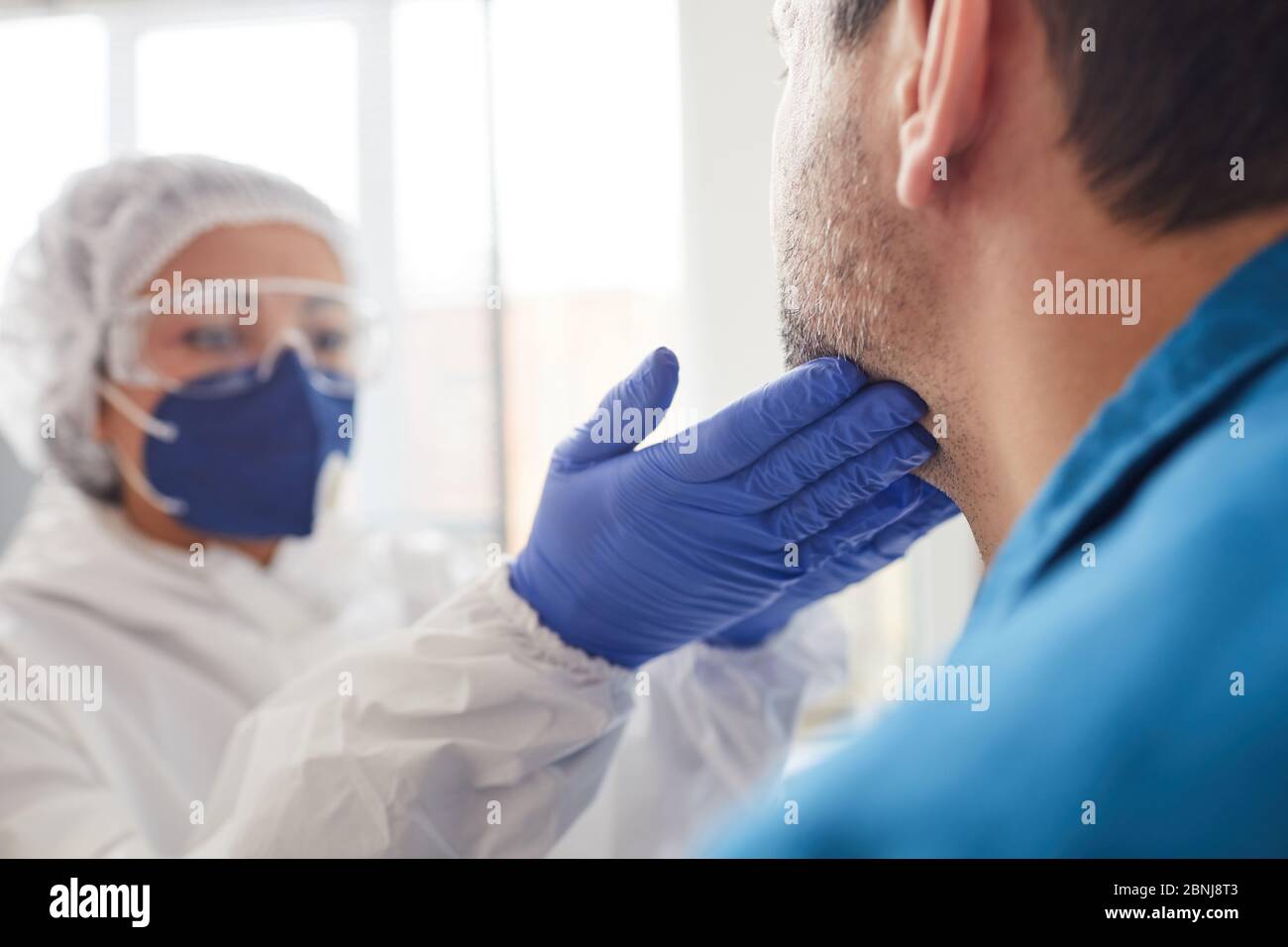 Gros plan d'une infirmière vêque de vêtements de protection examinant la gorge du patient pendant un examen médical à l'hôpital Banque D'Images