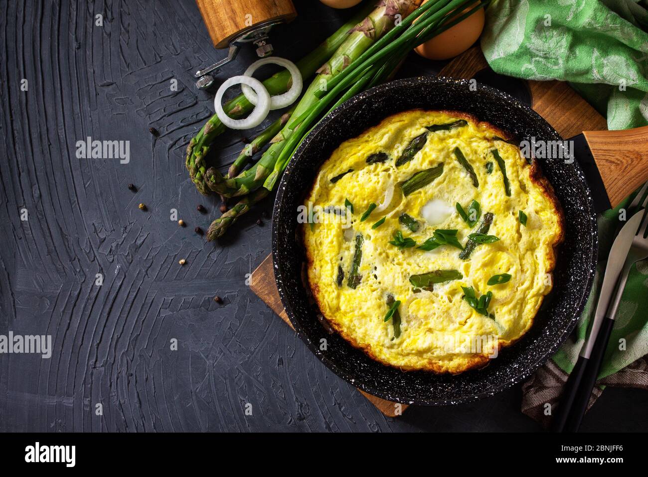 Omelette aux asperges saines. Omelette aux oeufs avec asperges et oignons dans une poêle en fonte sur un comptoir en pierre. Vue de dessus de l'arrière-plan de la mise à plat Copier l'espace. Banque D'Images