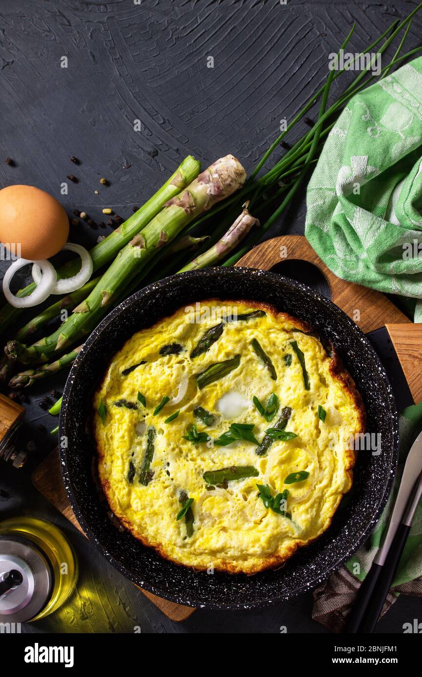 Omelette aux asperges saines. Omelette aux oeufs avec asperges et oignons dans une poêle en fonte sur un comptoir en pierre. Vue de dessus de l'arrière-plan de la mise à plat Copier l'espace. Banque D'Images